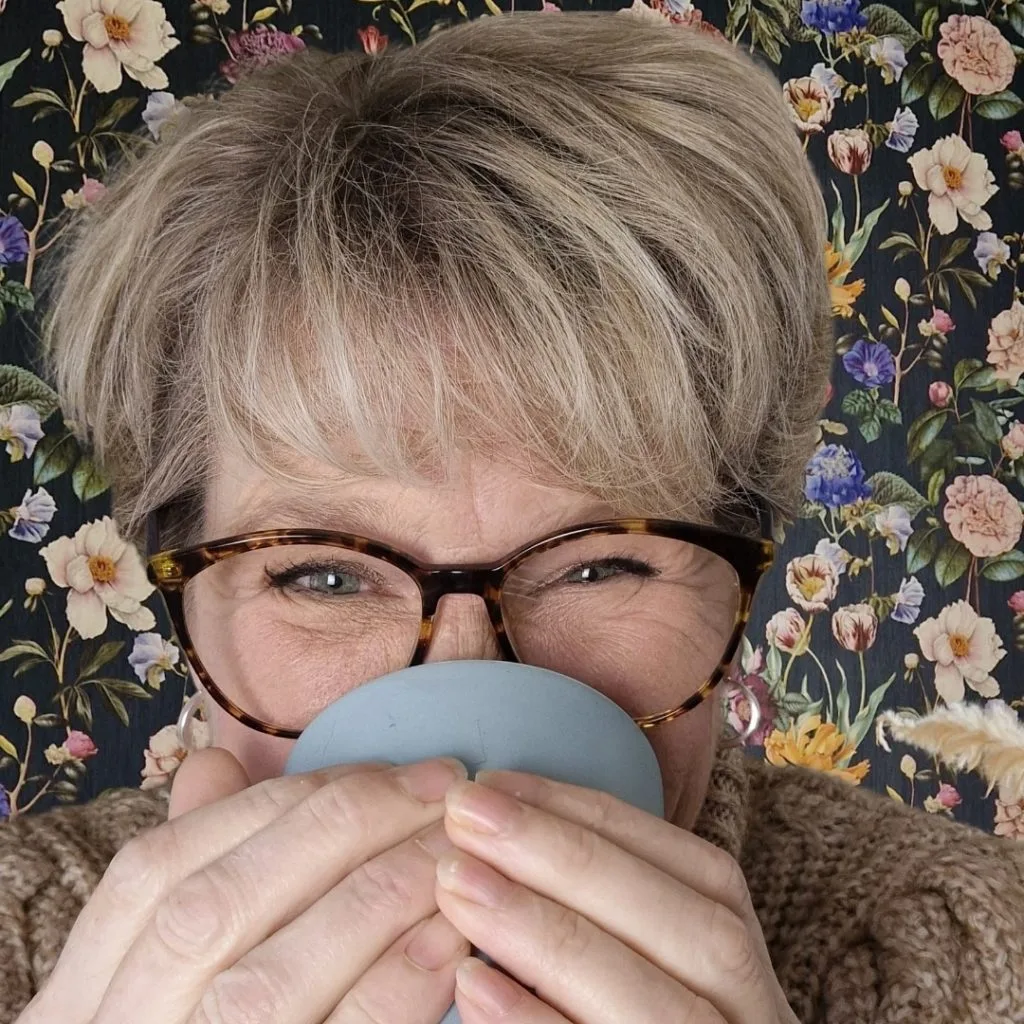 Portret van Mirjam van Coaching aan de Koffietafel met een koffiekopje voor haar gezicht, warme en huiselijke sfeer.