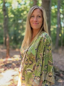 Irene, een dame met lang blond haar staat in het bos, de zon schijn op haar, ze draagt een groene kimono met bloemen print
