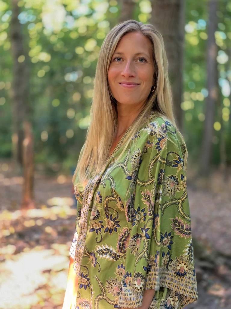 Irene, een dame met lang blond haar staat in het bos, de zon schijn op haar, ze draagt een groene kimono met bloemen print