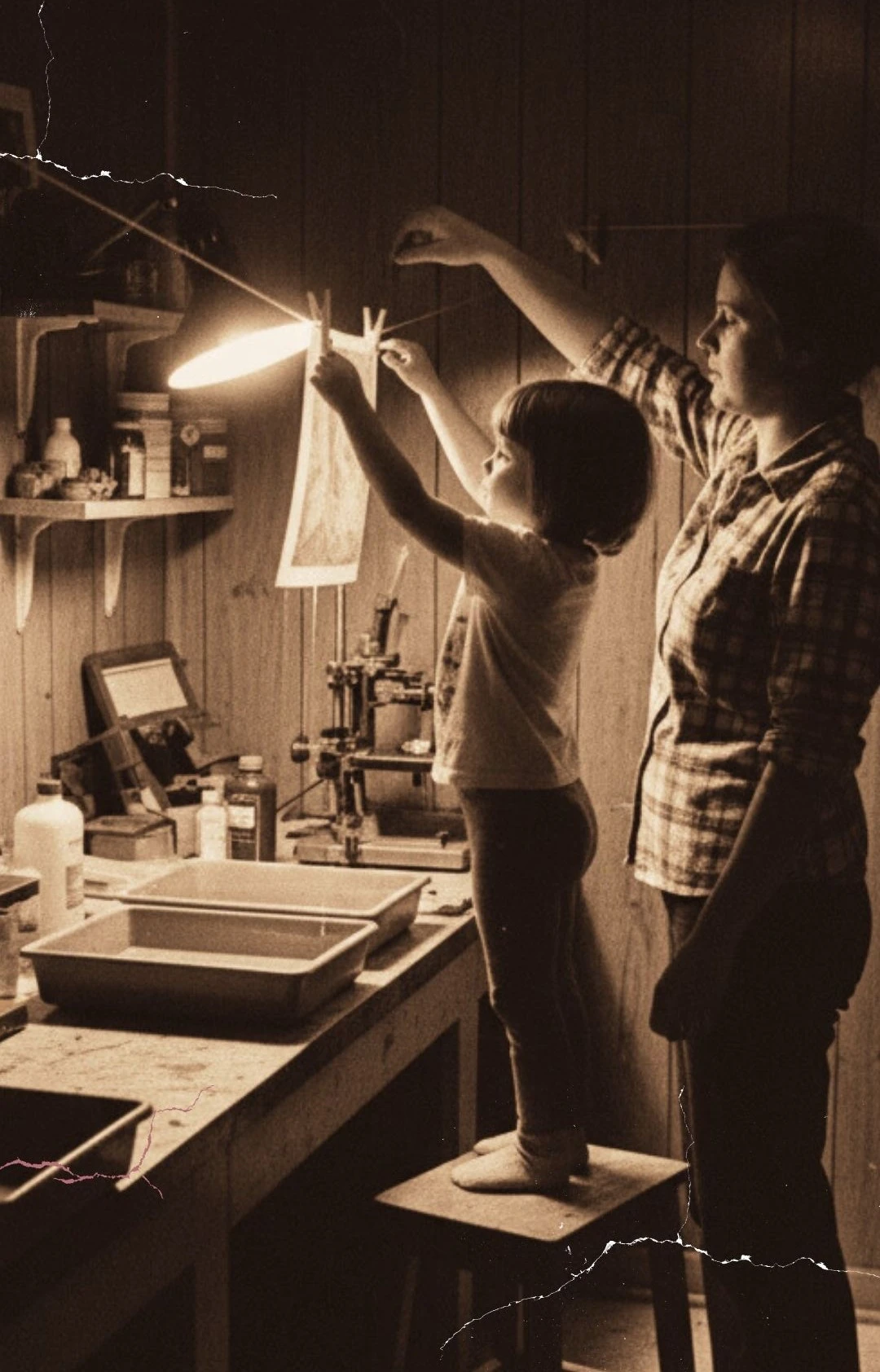 Klein meisje en haar moeder in een donkere kamer terwijl ze samen foto’s ontwikkelen en ophangen, begin van oog voor detail en gevoel voor licht en compositie.
