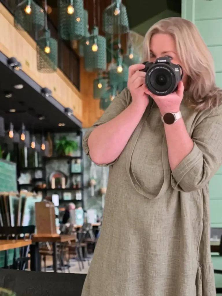 Marion van The Web Creator fotografeert met een professionele camera in een sfeervolle setting. Ze kijkt door de lens, gefocust op het vastleggen van de unieke energie en het verhaal van de ondernemer voor hun nieuwe website.