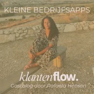 Een vrouw met lang donker krullend haar zit op blote voeten op een eenvoudig houten bankje. Ze draagt kleding met een zwart-wit patroon en kijkt rustig naar de camera. Achter haar ligt een weids heuvellandschap dat mooi wordt verlicht door de warme avondzon, met een laag stenen muurtje op de voorgrond.