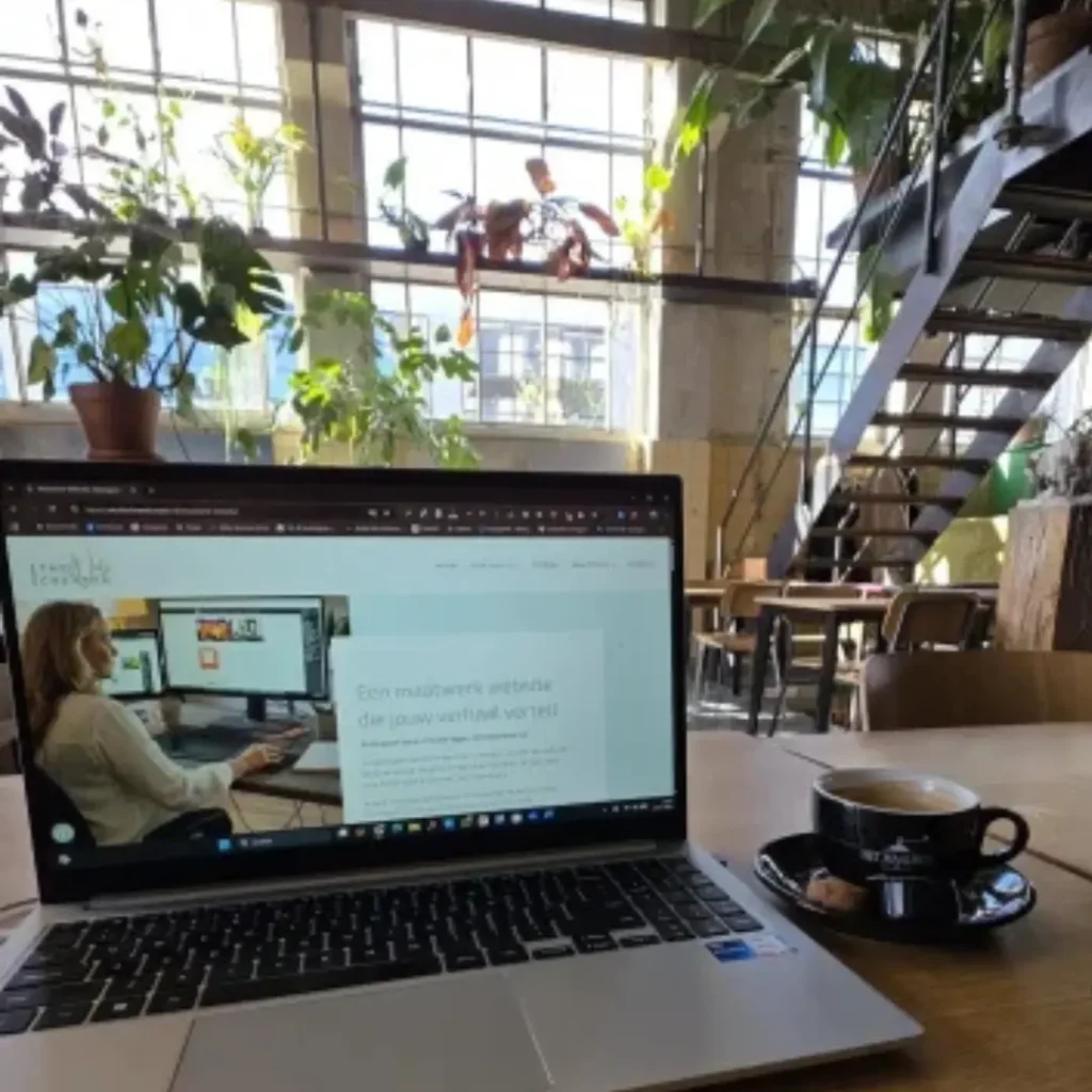 Laptop met de website van Studio The WebCreator geopend, op een houten tafel met een kopje koffie"